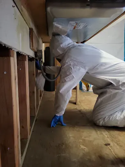 Technician in a protective suit working along flood-cut wall framing in a Little Elm home